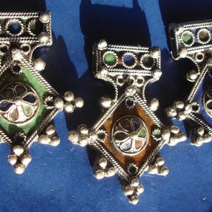 May include: Three silver pendants with intricate designs and colorful enamel accents. Each pendant features a central geometric shape with a different color scheme: green, brown, and blue.