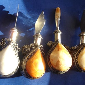 Pode incluir: Quatro frascos de perfume antigos de prata e âmbar com correntes de prata adornadas. Os frascos têm a forma de lágrima e contêm âmbar de diferentes cores.