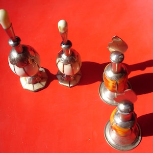 May include: Four decorative objects with metallic silver-toned bases and tops. Two items feature white, ribbed, rounded bodies with octagonal bases, while the other two have orange, textured, rounded bodies with circular metallic bases.