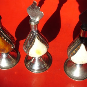 Puede incluir: Tres botellas decorativas con bases y tapas plateadas. Las botellas son de vidrio y tienen un acabado nacarado. Una botella tiene un diseño marrón y dorado, mientras que las otras dos tienen un diseño blanco y dorado.