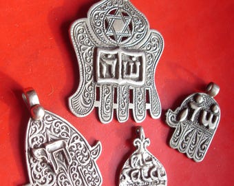 Pode incluir: Quatro pingentes de prata com designs intrincados, incluindo uma mão de Hamsa com uma Estrela de David, uma mão de Hamsa com letras hebraicas e duas mãos de Hamsa menores com letras hebraicas.