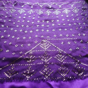 Puede incluir: Una tela morada con un patrón plateado. La tela tiene un diseño geométrico con pequeñas cuentas plateadas.