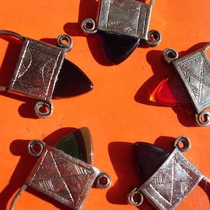 May include: Five silver pendants with different colored glass inserts. The pendants are shaped like a small box with a loop at the top. The glass inserts are red, purple, green, and black.