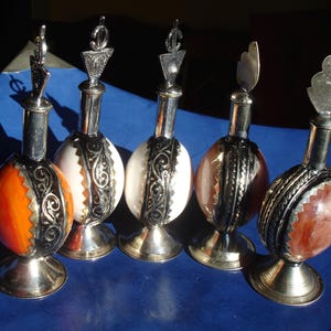 Pode incluir: Cinco garrafas decorativas com tampas prateadas e desenhos ornamentados. As garrafas são feitas de vidro e têm pedras de diferentes cores no interior. As garrafas são todas de tamanhos e formas diferentes.