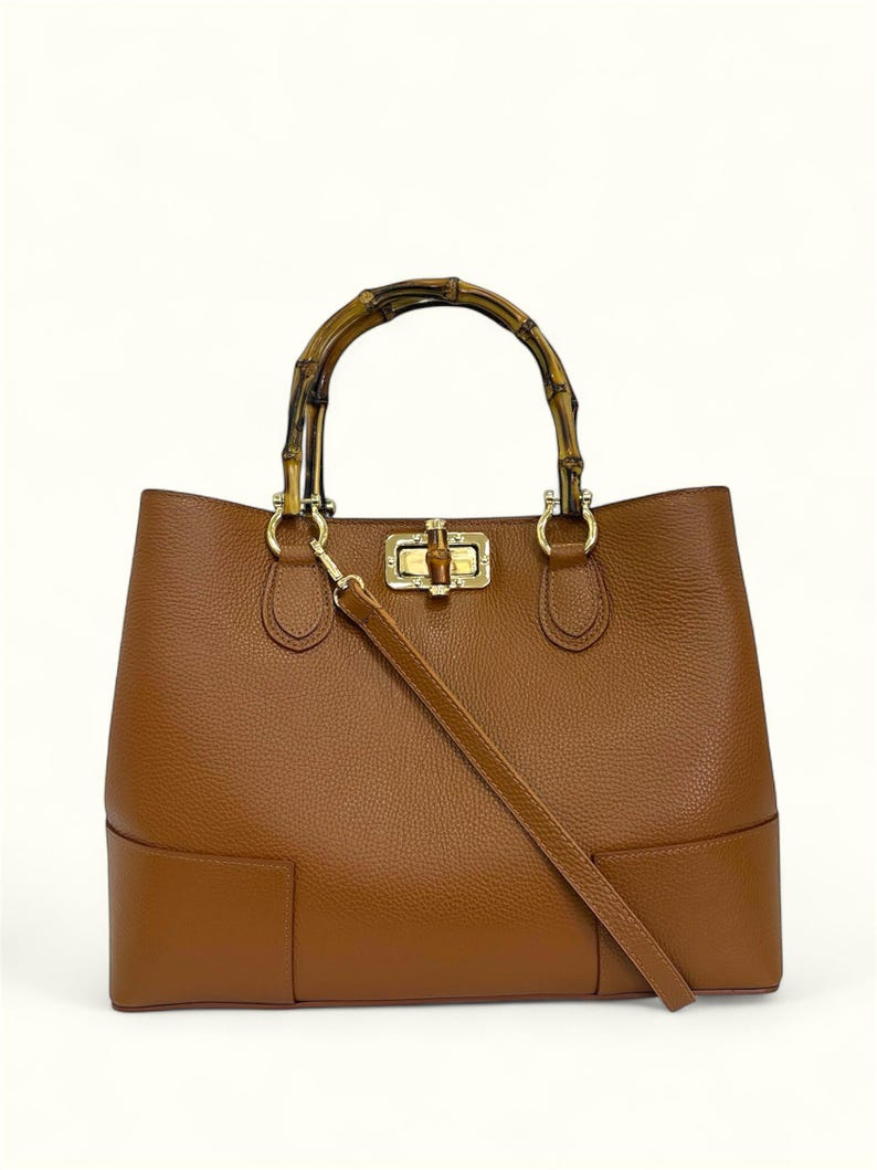 May include: A brown leather handbag with a textured surface, featuring a curved bamboo handle and a gold-toned metal turn-lock closure. The bag includes a detachable, matching brown leather shoulder strap attached to gold-toned hardware rings.