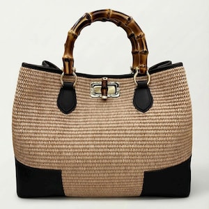 Pode incluir: Bolsa tote bege tecida com al&ccedil;a de bambu. A bolsa apresenta detalhes em couro preto e um fecho dourado. A al&ccedil;a &eacute; feita de bambu curvo. Dimens&otilde;es: aproximadamente 30 cm de largura.