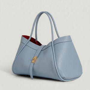K&ouml;nnte beinhalten: Hellblaue Ledertasche mit strukturiertem Design. Die Tasche hat zwei obere Griffe und einen Riemen mit goldfarbenem Verschluss. Der Innenraum ist mit rotem Stoff gef&uuml;ttert.