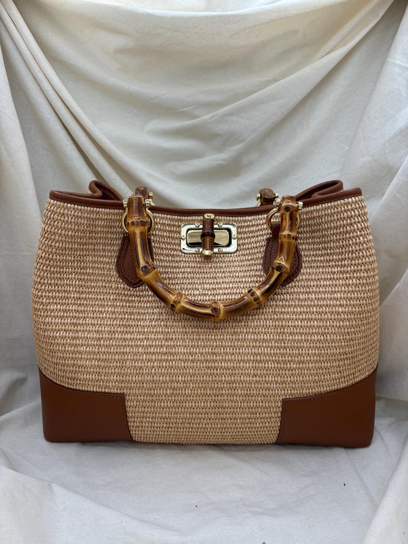 Pode incluir: Uma bolsa tote bege tecida com detalhes em couro castanho e uma al&ccedil;a de bambu. A bolsa tem formato retangular com fecho dourado e cantos em couro castanho. A al&ccedil;a &eacute; feita de bambu curvo.