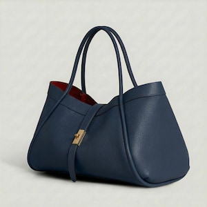 K&ouml;nnte beinhalten: Eine marineblaue Tragetasche mit strukturiertem Design. Die Tasche hat zwei obere Griffe und einen Riemenverschluss mit einem goldfarbenen Verschluss. Das Innenfutter ist rot.
