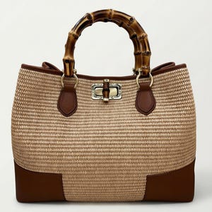 Pode incluir: Uma bolsa tote de palha tecida com uma al&ccedil;a de bambu. A bolsa apresenta detalhes em couro marrom na base e na borda, com um fecho dourado. A al&ccedil;a &eacute; feita de bambu curvo.
