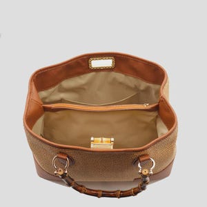Pode incluir: Vista aberta de uma mala tote castanha e bege com al&ccedil;as de bambu. A mala apresenta uma textura tecida nas laterais e acabamento em couro. O interior &eacute; bege com bolsos e fecho de correr. Um fecho dourado prende a mala.