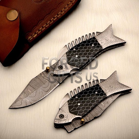 Hand-forged Damascus steel folding knife with a fish-shaped black honeycomb resin handle — this is genuine artisan craft, not a catalog item.