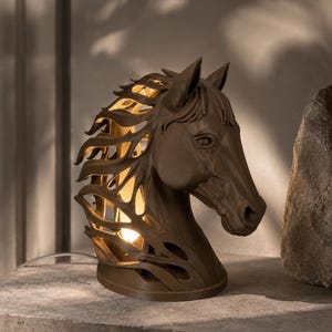 Peut inclure: Une lampe en forme de tête de cheval marron avec une crinière ajourée laissant passer la lumière d'une ampoule interne. La sculpture est fixée sur une base circulaire et présente des détails faciaux précis incluant oreilles, yeux et naseaux.
