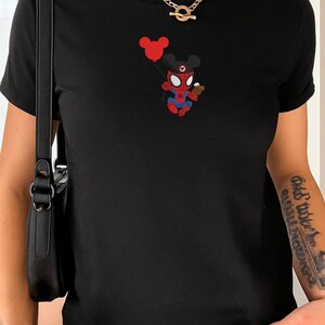 May include: Black t-shirt featuring a cartoon mashup of Spider-Man and Mickey Mouse holding a red balloon and a small treat. The graphic is in red, blue, and black. The shirt has short sleeves and a crew neck.