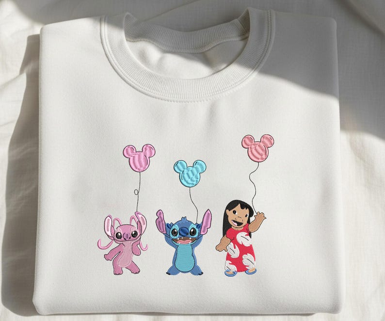 K&ouml;nnte beinhalten: Ein wei&szlig;es Sweatshirt mit Rundhalsausschnitt und einer Stickerei, die einen rosa Au&szlig;erirdischen, einen blauen Au&szlig;erirdischen und ein M&auml;dchen in einem roten Kleid zeigt. Jede Figur h&auml;lt eine Schnur mit einem Mickey-Maus-Ballon in passender Farbe.