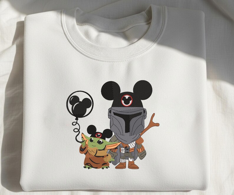 Op de afbeelding: Een wit sweatshirt met ronde hals en een grafische print van een klein groen wezen in een bruine mantel en een figuur in een grijs harnas, beide met zwarte Mickey Mouse-oren. Het kleine wezen houdt een zwarte Mickey Mouse-ballon vast.