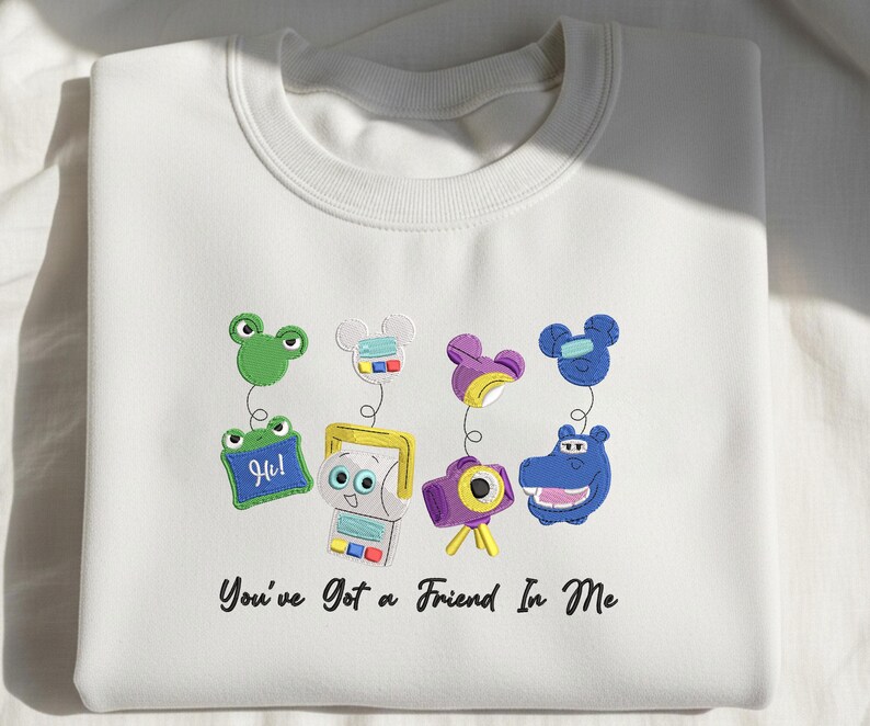 May include: A white crewneck sweatshirt featuring an embroidered design of four colorful characters with spring-like attachments and the text "You've Got a Friend In Me" printed in black script below the graphic elements on the front of the garment.