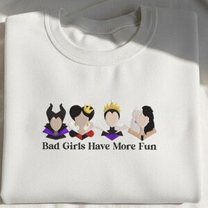 May include: White sweatshirt with embroidered cartoon images of four characters. The characters are in black, purple, red, and gold. The text "Bad Girls Have More Fun" is embroidered below the characters.