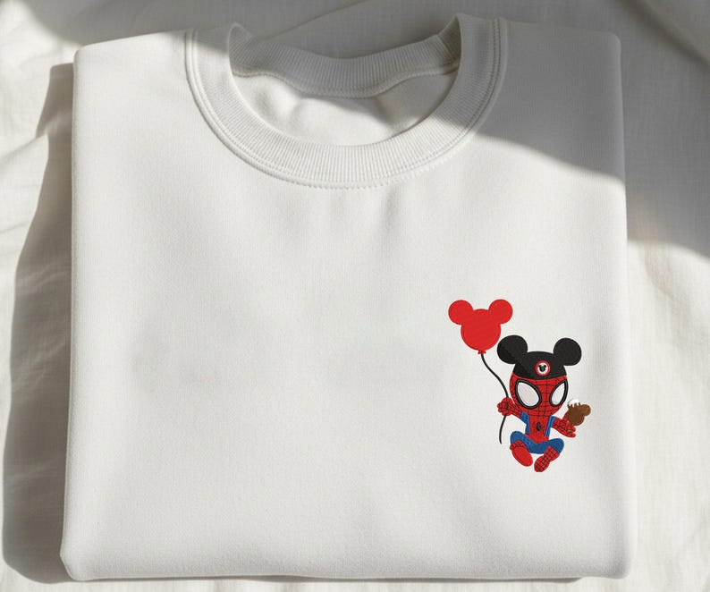 May include: White sweatshirt featuring a cartoon character mashup of Spider-Man and Mickey Mouse. The character is holding a red balloon and a small brown object. The design is in red, blue, black, and brown.