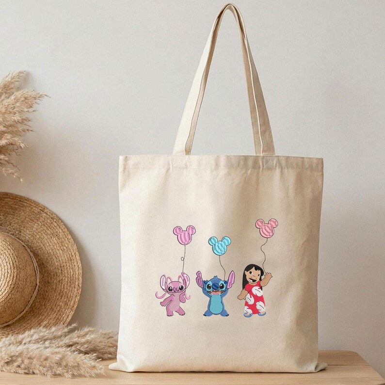 K&ouml;nnte beinhalten: Eine naturfarbene Canvas-Tragetasche mit einem grafischen Aufdruck, der ein rosa Alien, ein blaues Alien und ein M&auml;dchen in einem roten Blumenkleid zeigt. Jede Figur h&auml;lt einen Luftballon in Form eines Mauskopfes in Rosa, Blau oder Rosa.