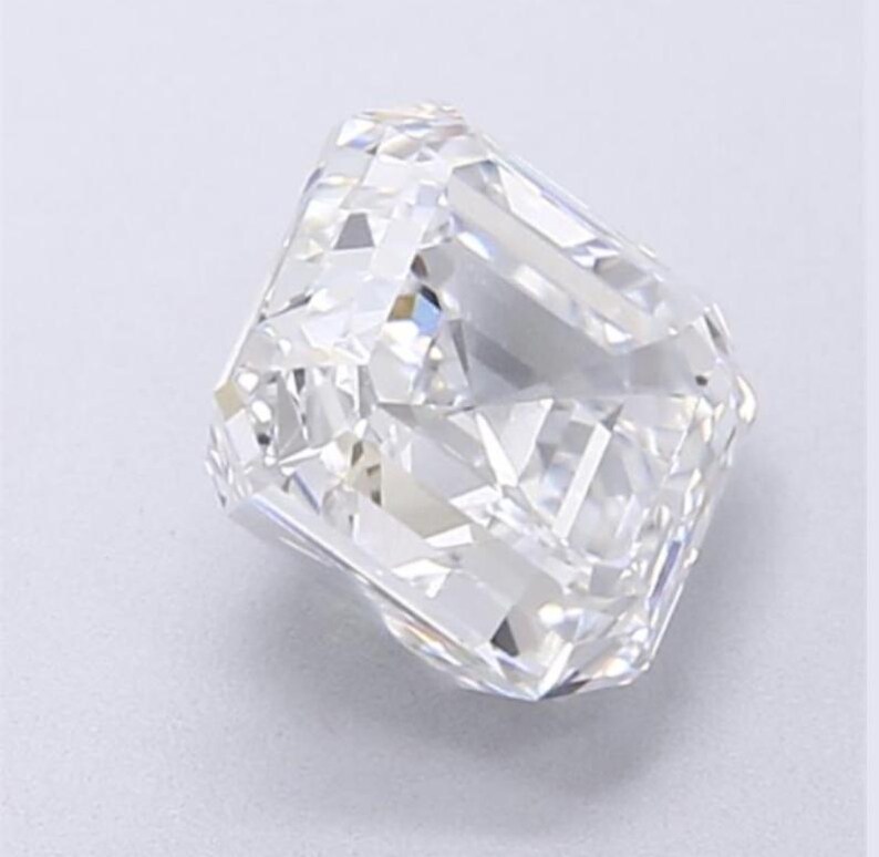 May include: A radiant-cut diamond with a brilliant, multifaceted surface. The colorless gemstone reflects light, showcasing its internal structure and clarity. The diamond's shape is rectangular with cut corners, a classic choice for jewelry.