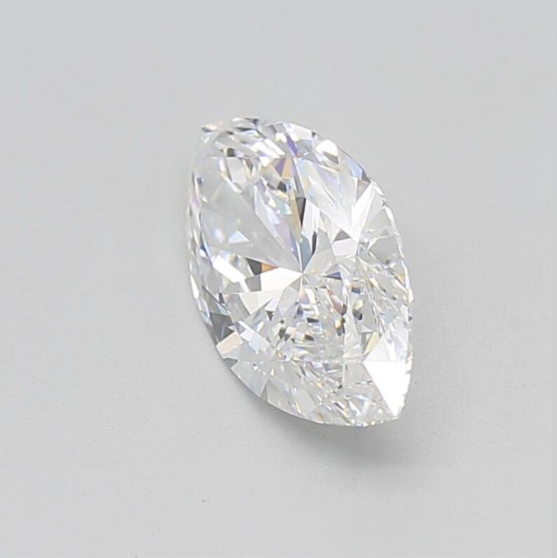 May include: A marquise-cut diamond with a brilliant, faceted surface. The colorless gemstone reflects light, showcasing its intricate internal structure. The elongated shape and pointed ends are characteristic of this diamond cut.