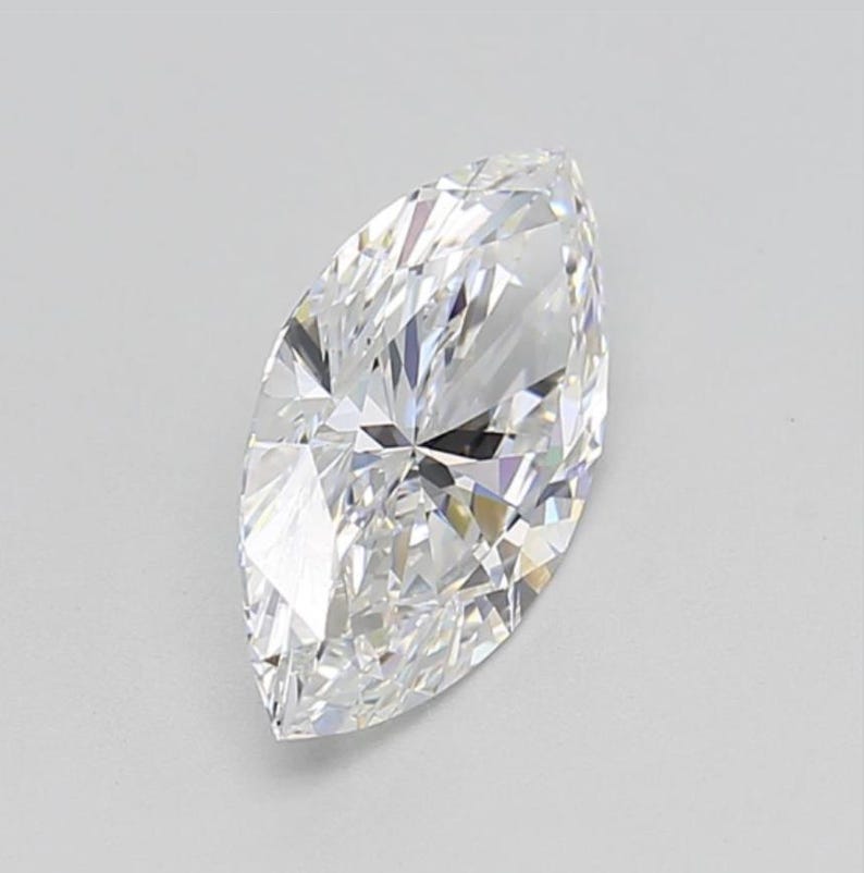 May include: A marquise-cut diamond, showcasing a brilliant, elongated shape. The gemstone is clear and colorless, with numerous facets that reflect light, creating a sparkling effect. The diamond is set against a plain, light background.