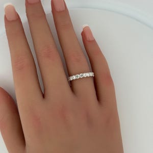 Puede incluir: Primer plano de una mano con un anillo de diamantes de la eternidad. El anillo presenta una fila continua de diamantes de talla redonda engastados en una banda de metal blanco. Los diamantes brillan, reflejando la luz. Es una joya cl&aacute;sica.
