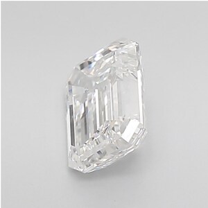 May include: A clear, emerald-cut diamond with a rectangular shape and beveled corners. The facets reflect light, creating a brilliant sparkle. The diamond is set against a plain white background, highlighting its clarity and brilliance.