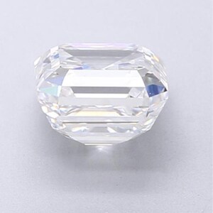 May include: A clear, faceted gemstone with an emerald cut. The gem has a rectangular shape with cut corners and a brilliant, reflective surface. The facets create a play of light and shadow, giving the stone a sparkling appearance.