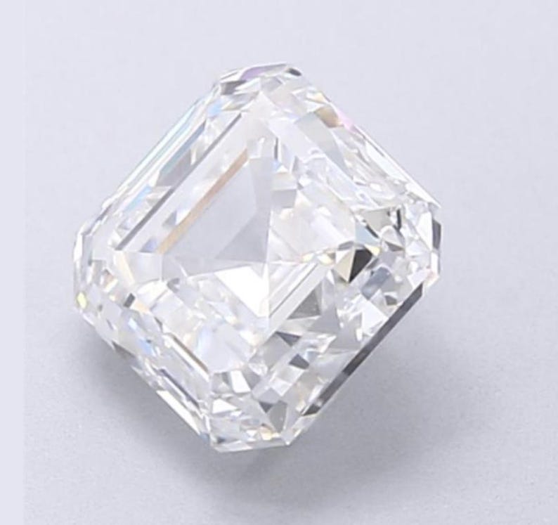 May include: A clear, radiant-cut diamond with a rectangular shape and beveled corners. The facets reflect light, creating a brilliant sparkle. The gemstone is set against a light background, showcasing its clarity and brilliance.