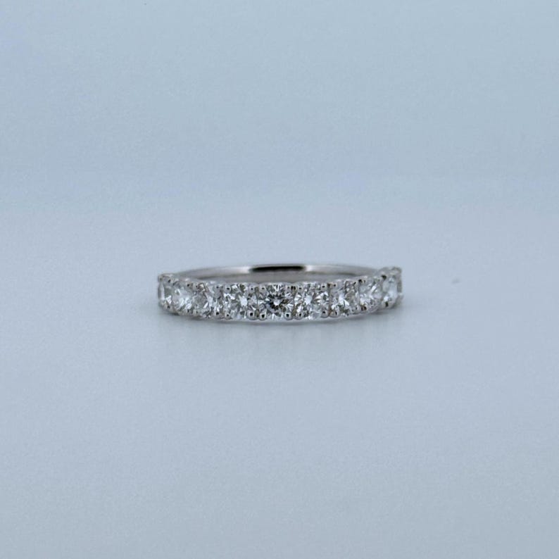 Puede incluir: Un anillo de plata con una fila continua de piedras preciosas redondas y claras. El anillo est&aacute; engastado sobre un fondo azul claro, resaltando el brillo de las piedras. Un dise&ntilde;o cl&aacute;sico, adecuado para diversas ocasiones. El ancho del anillo es de aproximadamente 0,2 cm.