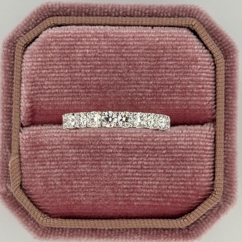 Puede incluir: Un anillo de plata con una fila de piedras preciosas redondas y transparentes. El anillo se presenta en un joyero de terciopelo rosa. Las piedras preciosas brillan. Un dise&ntilde;o cl&aacute;sico, adecuado para diversas ocasiones.