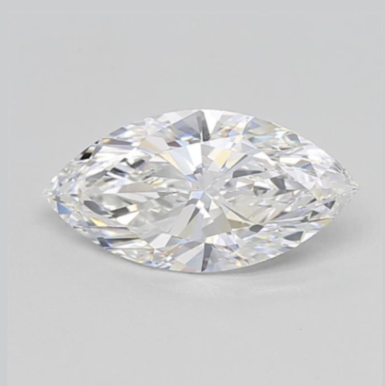 May include: A marquise-cut diamond with a brilliant, faceted surface. The colorless gemstone is set against a white background, showcasing its clarity and sparkle. The elongated shape of the diamond is prominent.