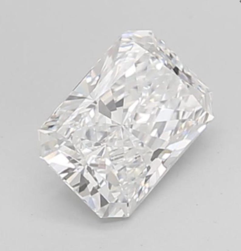 May include: A rectangular radiant-cut diamond. The colourless gemstone is highly faceted, reflecting light to create a brilliant sparkle. The diamond is set against a plain, light background.