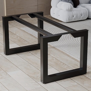 May include: A black metal table base featuring two rectangular side frames connected by two horizontal support bars. The structure is constructed from square tubing with a matte finish, designed to support a tabletop surface.