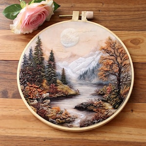 Könnte beinhalten: Runde Holzstickerei mit einer detaillierten Landschaftsdarstellung. Ein Fluss fließt durch ein Tal, im Hintergrund Berge und Bäume in Herbstfarben. Eine rosa Rose liegt auf der Holzoberfläche. Der Durchmesser beträgt ca. 20 cm.