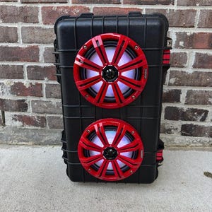 May include: A black speaker system with two red speakers. The speakers have a starburst design and are mounted on the front of the case. The speakers have a white and blue light. The case has red accents.