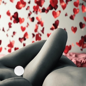 May include: A grayscale image featuring a person's body with a white circle. The background is a white wall adorned with scattered red heart shapes. The scene evokes a sense of romance and intimacy.