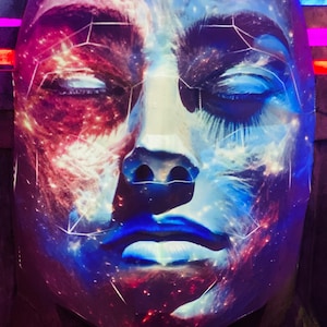 May include: A close-up of a face sculpture with closed eyes, featuring a cosmic design in shades of blue, red, and white. The artwork has a smooth surface and is illuminated with vibrant colors, creating a celestial effect. The sculpture's features are clearly defined.
