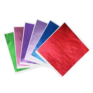 Puede incluir: Una colección de hojas de papel de aluminio metálico de colores en tonos verdes, rosas, morados, azules y rojos. Cada hoja cuadrada está montada sobre un respaldo blanco, creando una vibrante exhibición de colores. El papel de aluminio tiene una superficie texturizada y reflectante.