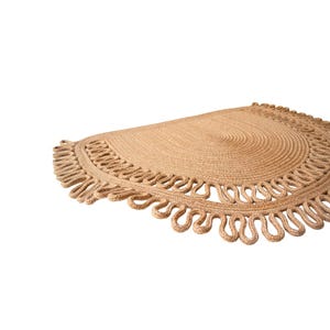 May include: A half-circle jute rug with a natural tan color. The rug features a spiral design in the center and a decorative looped edge. This rug is suitable for indoor use and adds a touch of natural texture to any space.