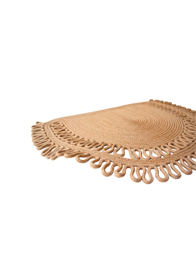 May include: A half-circle jute rug with a natural tan color. The rug features a spiral design in the center and a decorative looped edge. This rug is suitable for indoor use and adds a touch of natural texture to any space.