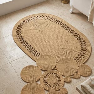 May include: Oval-shaped jute bath mat with a decorative border, accompanied by several matching circular coasters. The natural beige tones of the rug and coasters create a cohesive and earthy aesthetic, suitable for a bathroom setting.