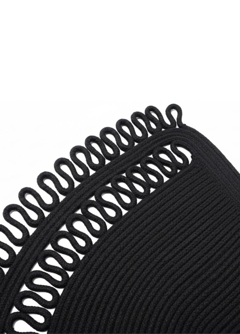 May include: Close-up of a black, textured rug with a unique design. The rug features a looped border and a ribbed interior, creating a visually interesting pattern. The dark color and detailed texture suggest a durable and stylish home decor item.