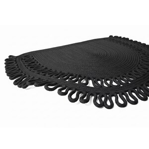 May include: A black, semi-circular woven placemat with a decorative looped edge. The placemat has a textured surface and a simple, elegant design. The item is suitable for home decor.