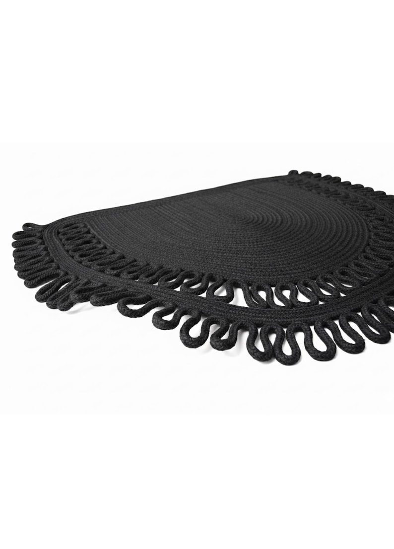 May include: A black, semi-circular woven placemat with a decorative looped edge. The placemat has a textured surface and a simple, elegant design. The item is suitable for home decor.