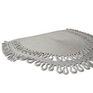 May include: A light gray, semi-circular rug with a looped edge design. The rug is made of a woven material and has a textured surface. The rug's diameter is approximately 30 inches.
