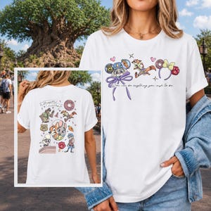 K&ouml;nnte beinhalten: Ein wei&szlig;es Kurzarm-T-Shirt mit Grafiken der Zootopia-Figuren und dem Text "You can be anything you wish to be." Das Design zeigt Illustrationen von Judy Hopps, Nick Wilde und Mausohren sowie eine detaillierte Collage auf der R&uuml;ckseite.