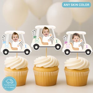 Könnte beinhalten: Drei Cupcakes mit weißem Zuckerguss, jeweils mit einem Golfwagen-förmigen Aufsatz mit einem Babygesicht. Die cremefarbenen Golfwagen haben schwarze Räder und die Nummer 1. Der Text "ANY SKIN COLOR" ist sichtbar.